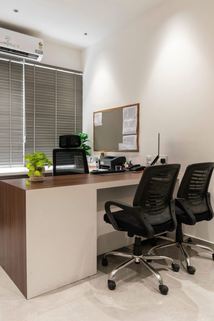 Office workspace with a timber desk, mesh chairs and a noticeboard by the window